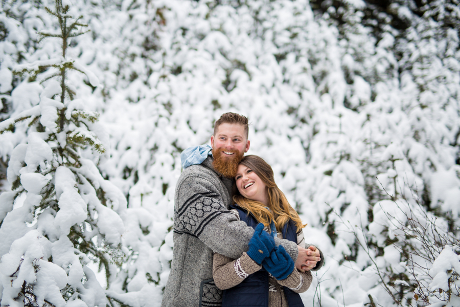 couple hugging in the snow while cozy sweaters 